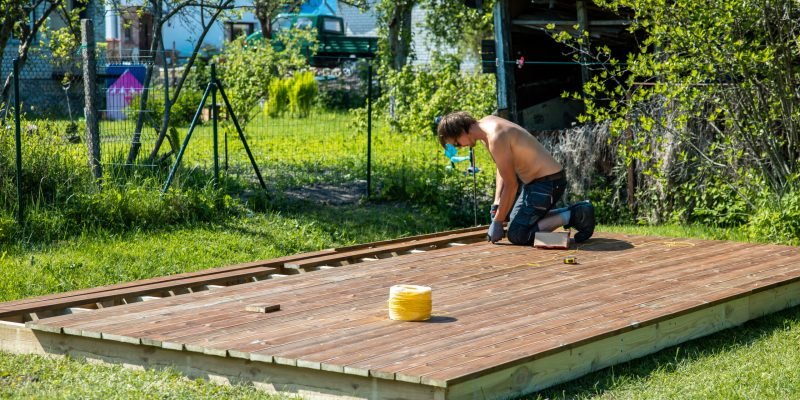 Deck construction, builder hand with electric screwdriver installing impregnated wooden boards